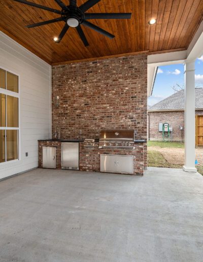 An outdoor patio featuring a built-in grill and storage under a covered ceiling with a fan.