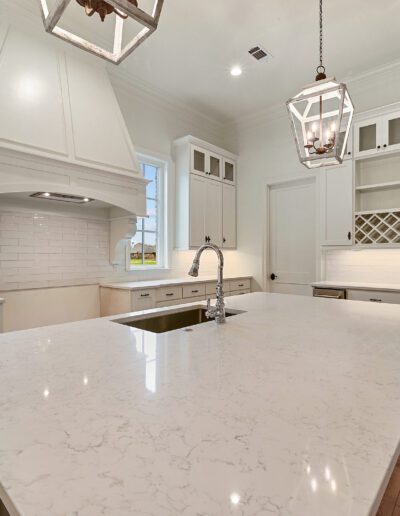 Spacious kitchen with modern white cabinetry, marble countertops, and pendant lighting.