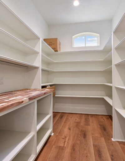A spacious, empty walk-in closet with white shelving and a wooden countertop under a small arched window.