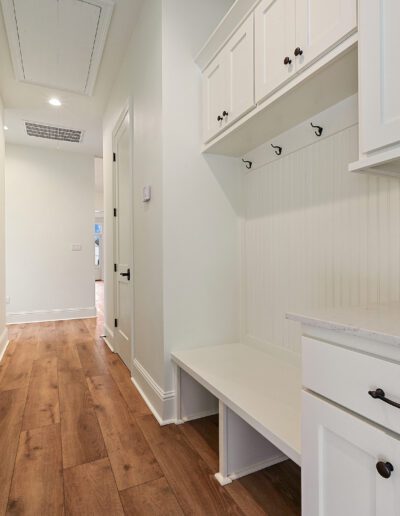 A clean and bright hallway featuring built-in white storage cabinets and a wooden bench with dark hardware on the doors.