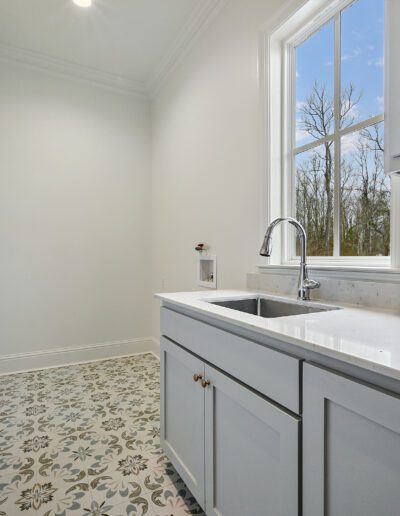 A bright, empty laundry room with white walls, floral patterned flooring, and a sink with gray cabinetry.