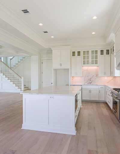 Spacious modern kitchen with white cabinetry and light wood flooring leading into an adjoining room with staircase.