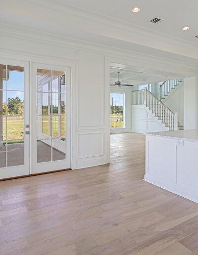 Spacious, modern kitchen with white cabinetry, a central island, and hardwood floors, leading to an adjoining room through french doors.