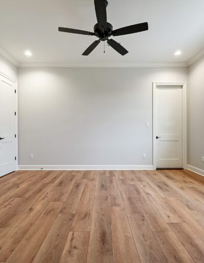 Empty room with hardwood flooring, white walls, and a ceiling fan.