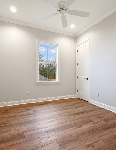 An empty room with hardwood floors, a closed white door, and a single window letting in natural light.