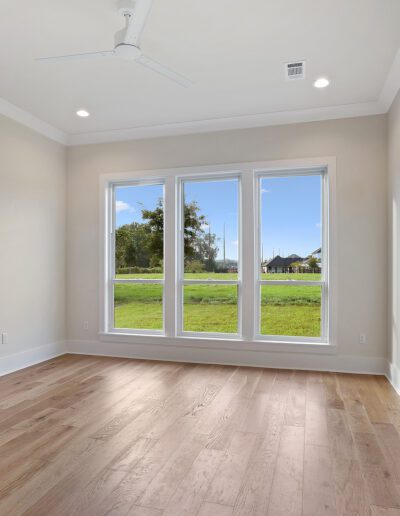 Bright empty room with hardwood floors and large windows overlooking a green field.