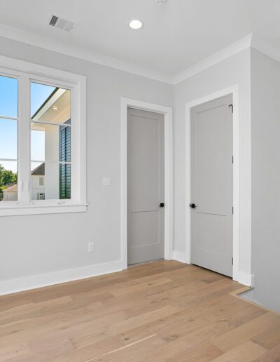 Bright and empty room with hardwood floors, white walls, and two closed doors.