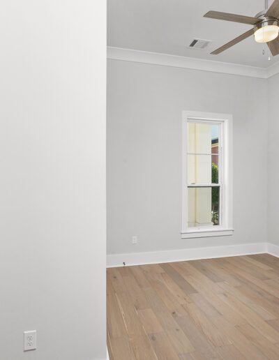Empty room with hardwood floors, white walls, and a ceiling fan near a window.
