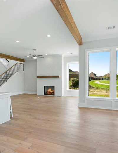 Spacious, modern living room with fireplace and open kitchen area, featuring large windows and wooden ceiling beams.