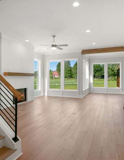 Modern empty living space with wooden floors, a staircase on the left, and a kitchen island visible to the right.