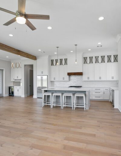 Modern kitchen with white cabinetry, stainless steel appliances, and wooden beams, featuring a central island with bar stools.
