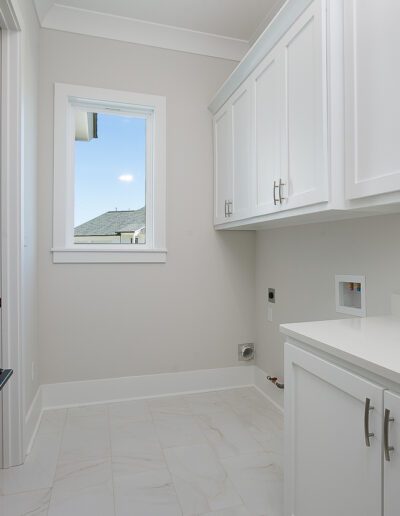A modern laundry room featuring white cabinetry, marble flooring, and a small window letting in daylight.