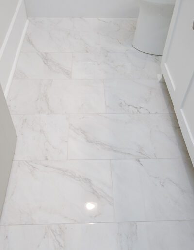 Modern bathroom with white marble floor tiles and white cabinetry.