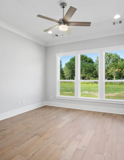 Empty room with hardwood floors, large windows, and a ceiling fan.