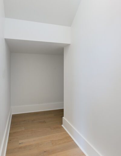An empty, narrow space with white walls and wooden flooring.