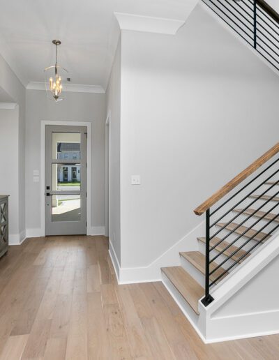 Modern home entryway with a wooden floor, white walls, and a staircase with black metal balusters.