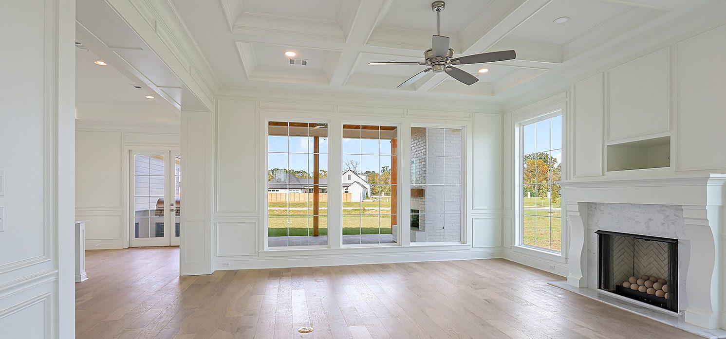 Spacious, empty room with a coffered ceiling, large windows, and a fireplace.
